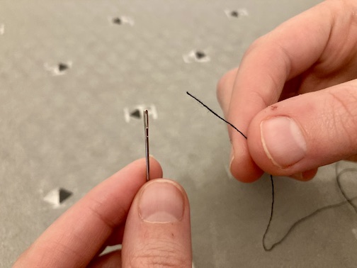 A person holding a needle and a strand of thread