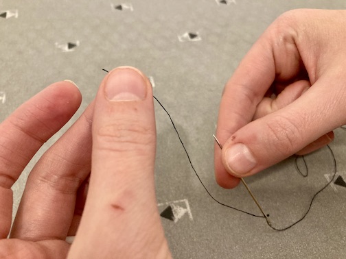 One hand holding the end of the thread above the needle the other hand is holding