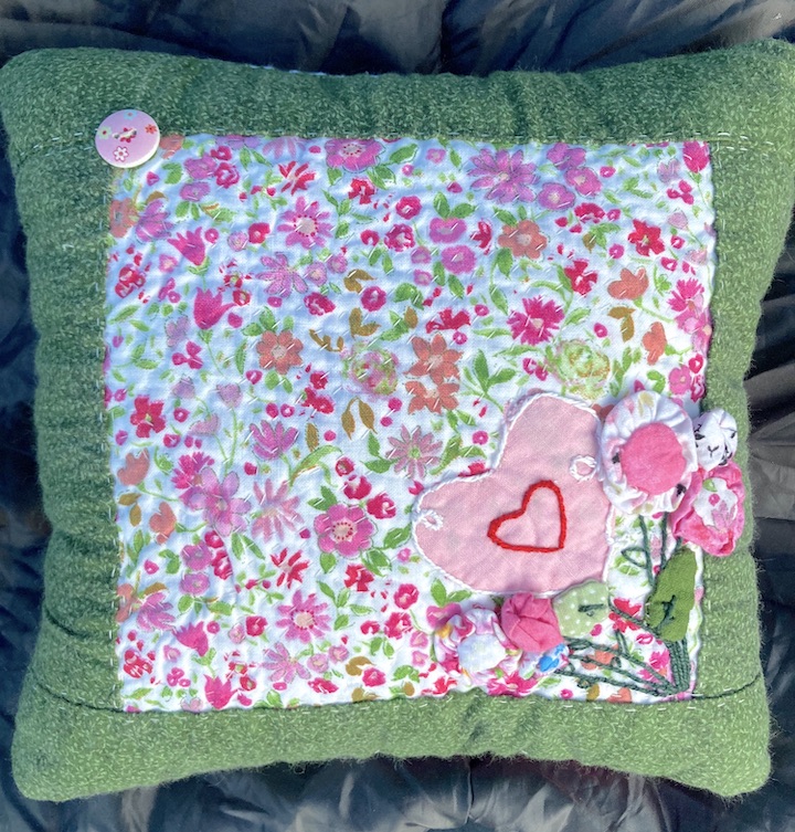 A green and pink hand sewed pillow using the basic hand stitches. With flowers sewn on the front. How To Sew Basic Hand Stitches