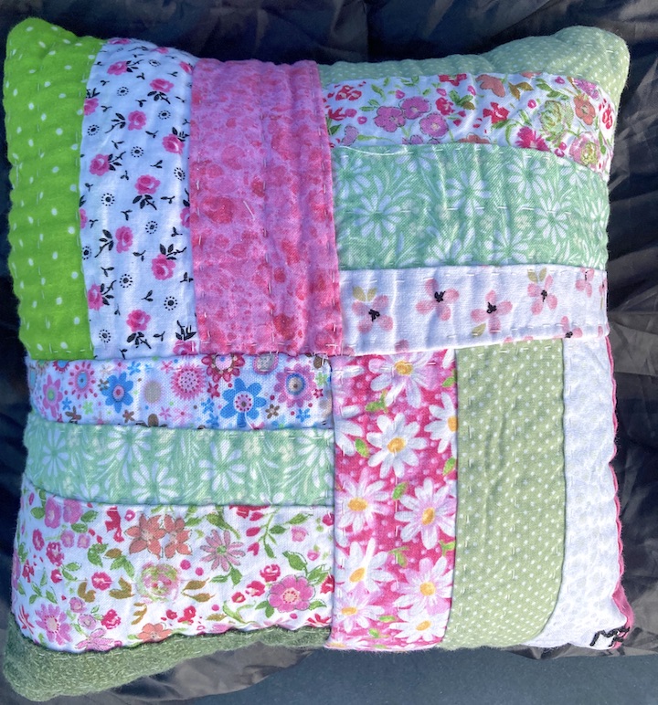A green and pink hand sewed pillow using the basic hand stitches.