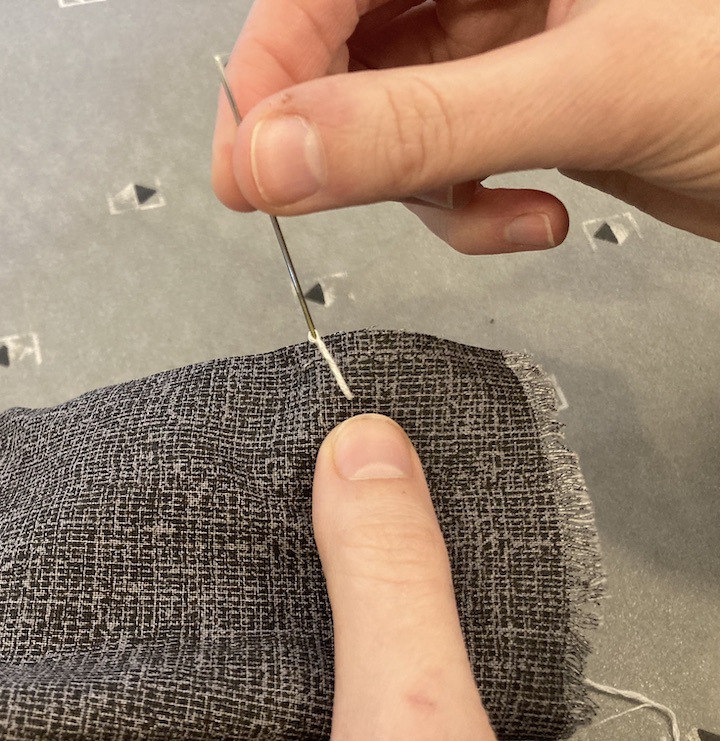 A needle attached to thread going through the fabric
