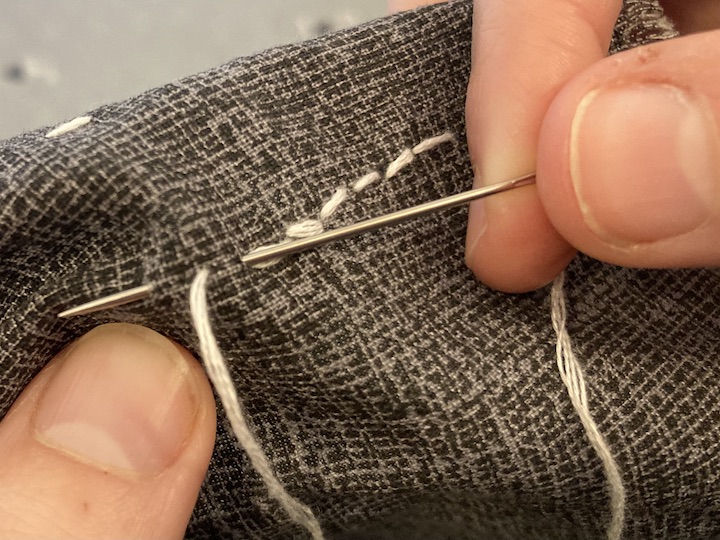 A needle and thread weaved into the fabric creating the next backstitch