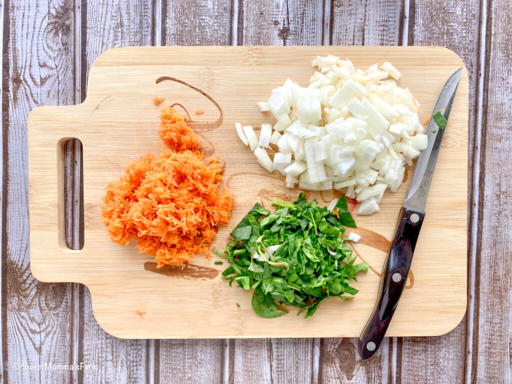 shredded carrots, chopped onion and spinach on a chopping board with knife.